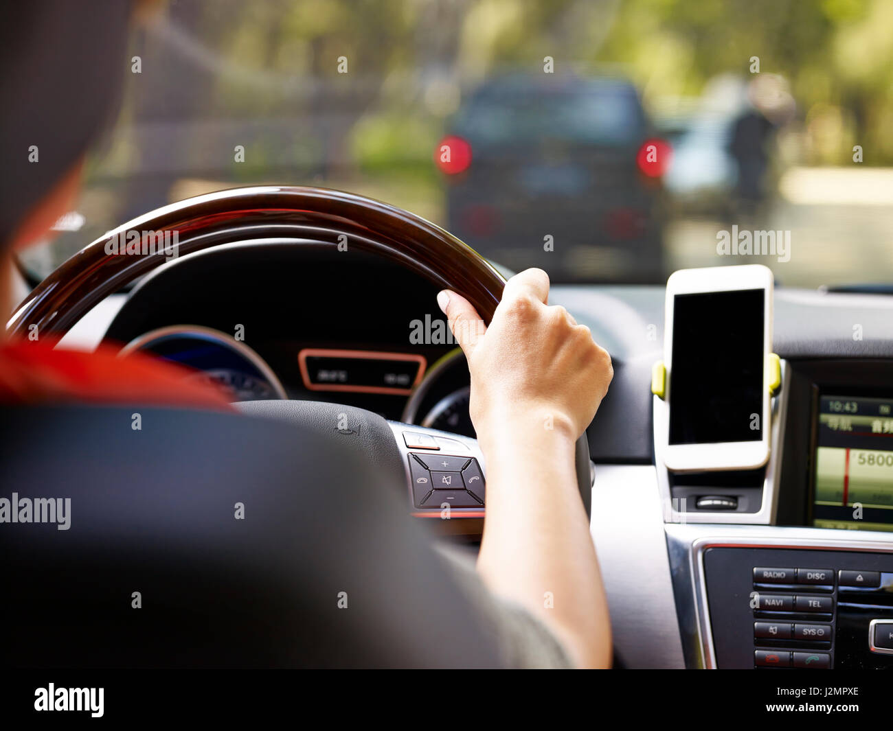 La mano di una donna che tiene il volante di guida di un veicolo con un cellulare montato sul cruscotto. Foto Stock