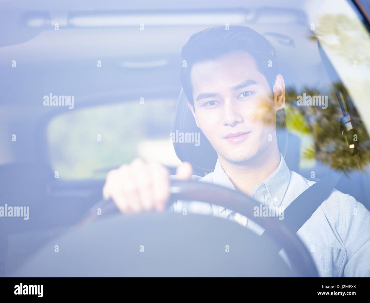 Giovani asiatici uomo alla guida di un veicolo visto attraverso il vetro del parabrezza. Foto Stock
