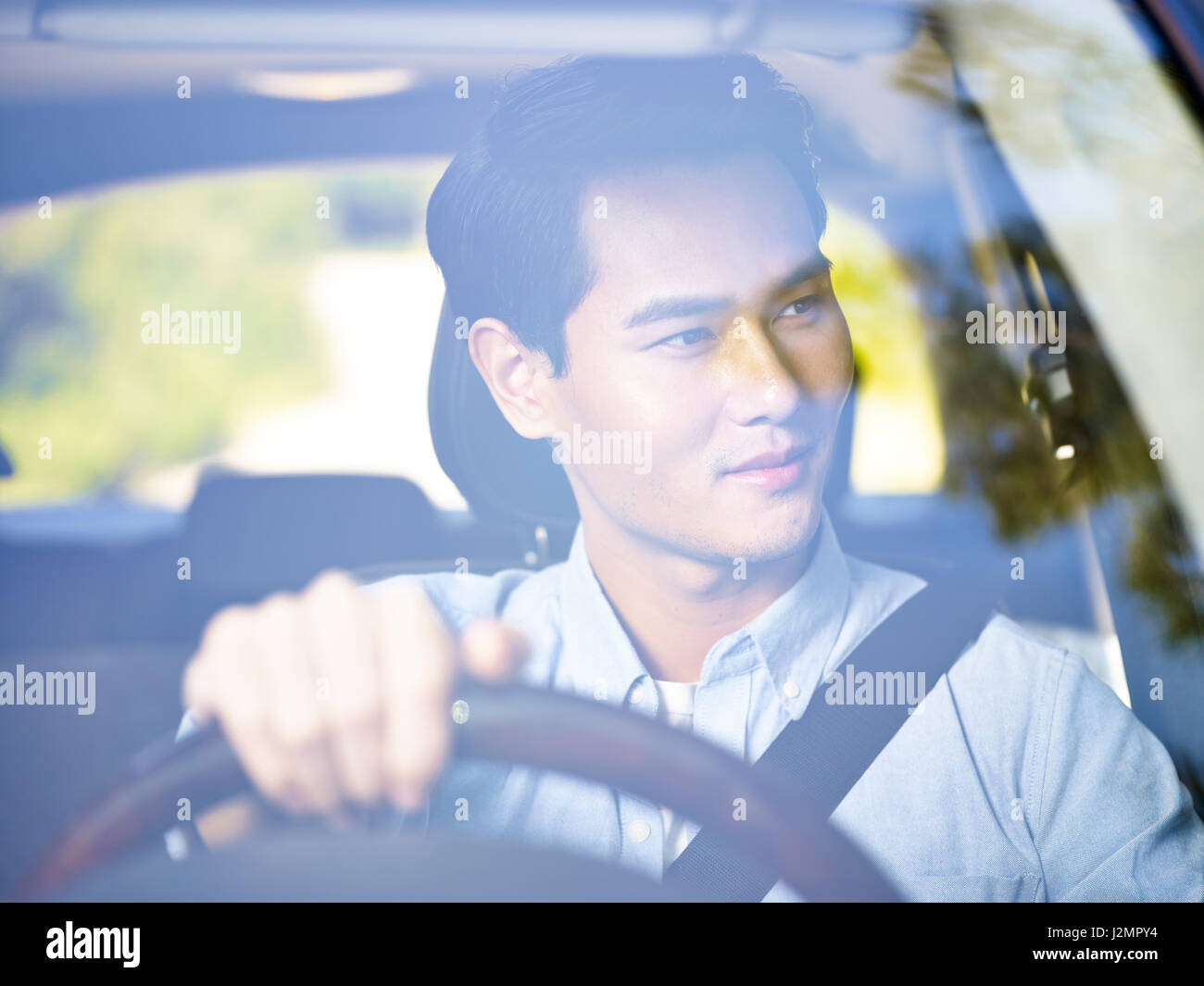 Giovani asiatici uomo alla guida di un veicolo, guardando paesaggi, visto attraverso il vetro del parabrezza. Foto Stock