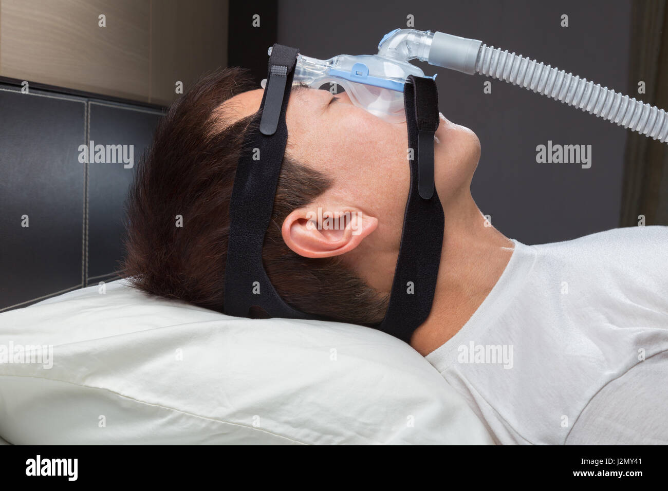 Uomo asiatico con apnea nel sonno usando macchina CPAP, indossando maschera copricapo per il collegamento al tubo di aria Foto Stock