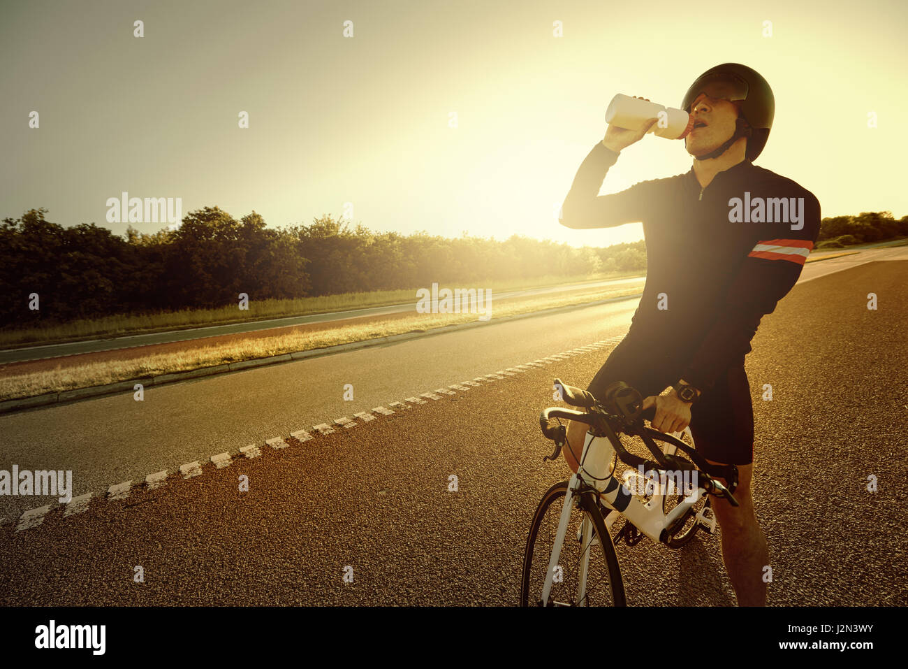 Montare la persona a riposo e acqua potabile dalla bottiglia seduto su una bicicletta di sera. Foto Stock