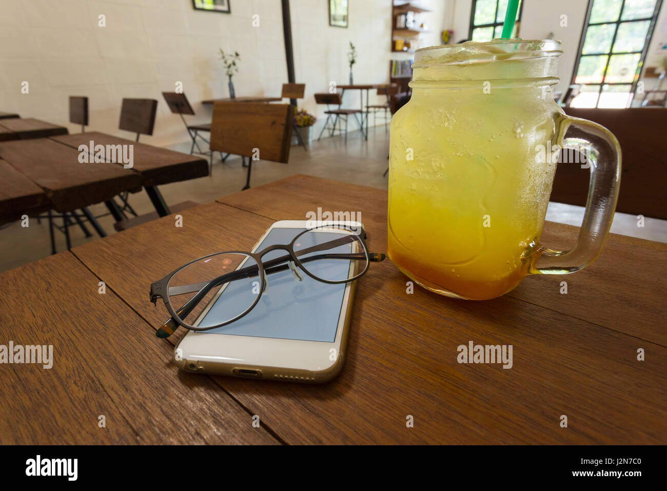 Un paio di occhiali seduto sul telefono accanto a una bevanda fredda sul tavolo di legno in una caffetteria, il fuoco selettivo su occhiali Foto Stock