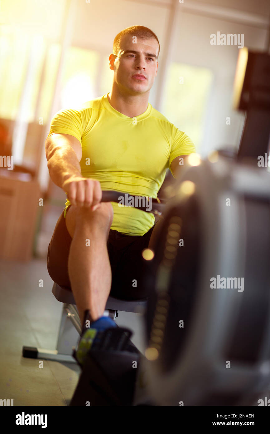 Giovane uomo che lavora sulla macchina di riga in studio fitness Foto Stock