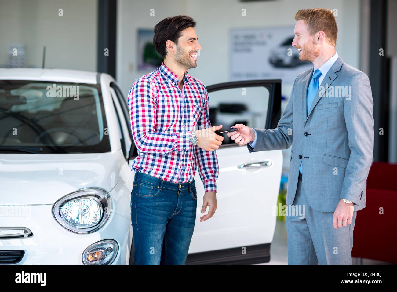 Situazione delle vendite in una concessionaria auto, il concessionario dando la chiave di auto presso i giovani di sesso maschile, Foto Stock