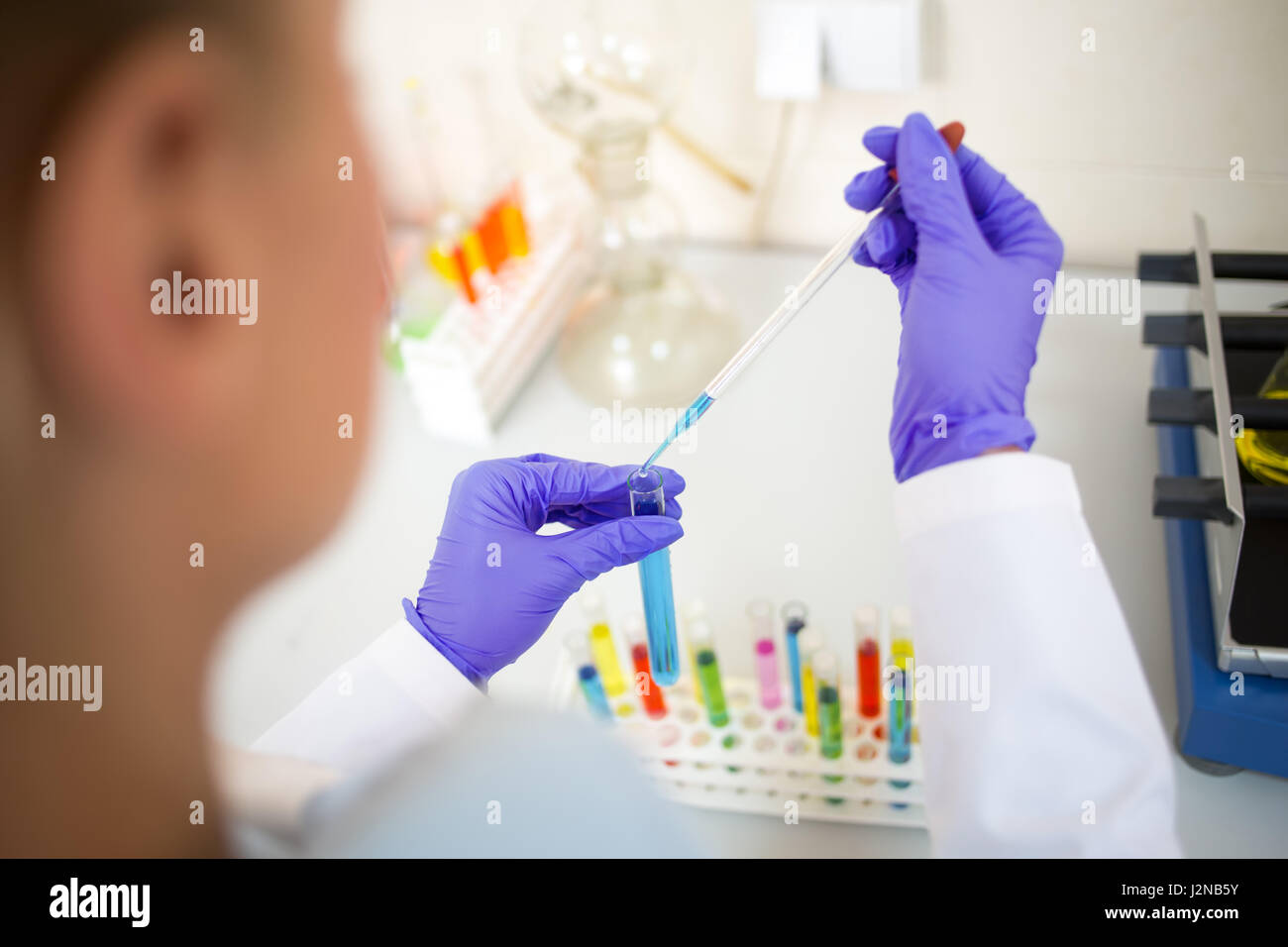 Vista ravvicinata del tecnico di laboratorio di campionamento di liquidi colorati con pipetta di vetro Foto Stock