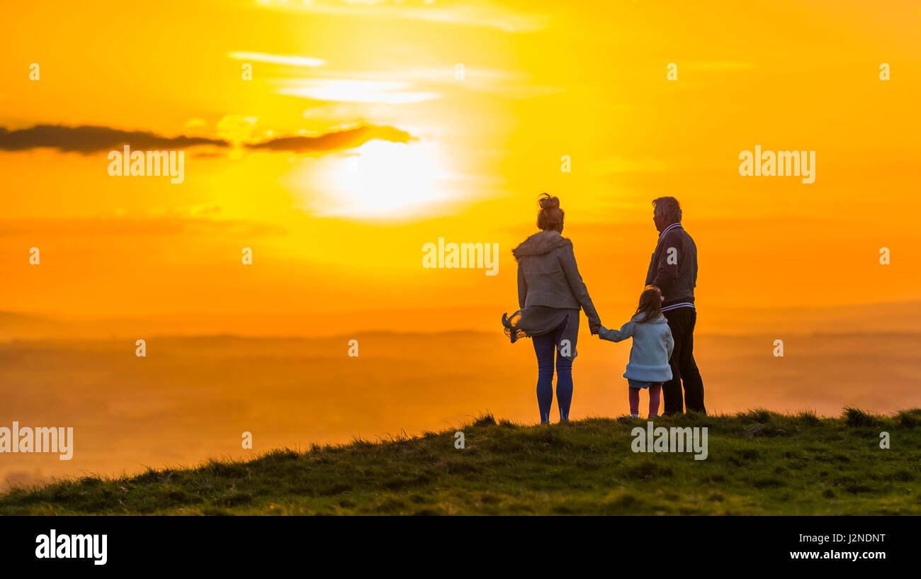 Piccola famiglia in piedi su una collina a guardare il tramonto mentre si tiene le mani. Concetto di stare insieme. Concetto di sempre. Il concetto di vicinanza. Foto Stock