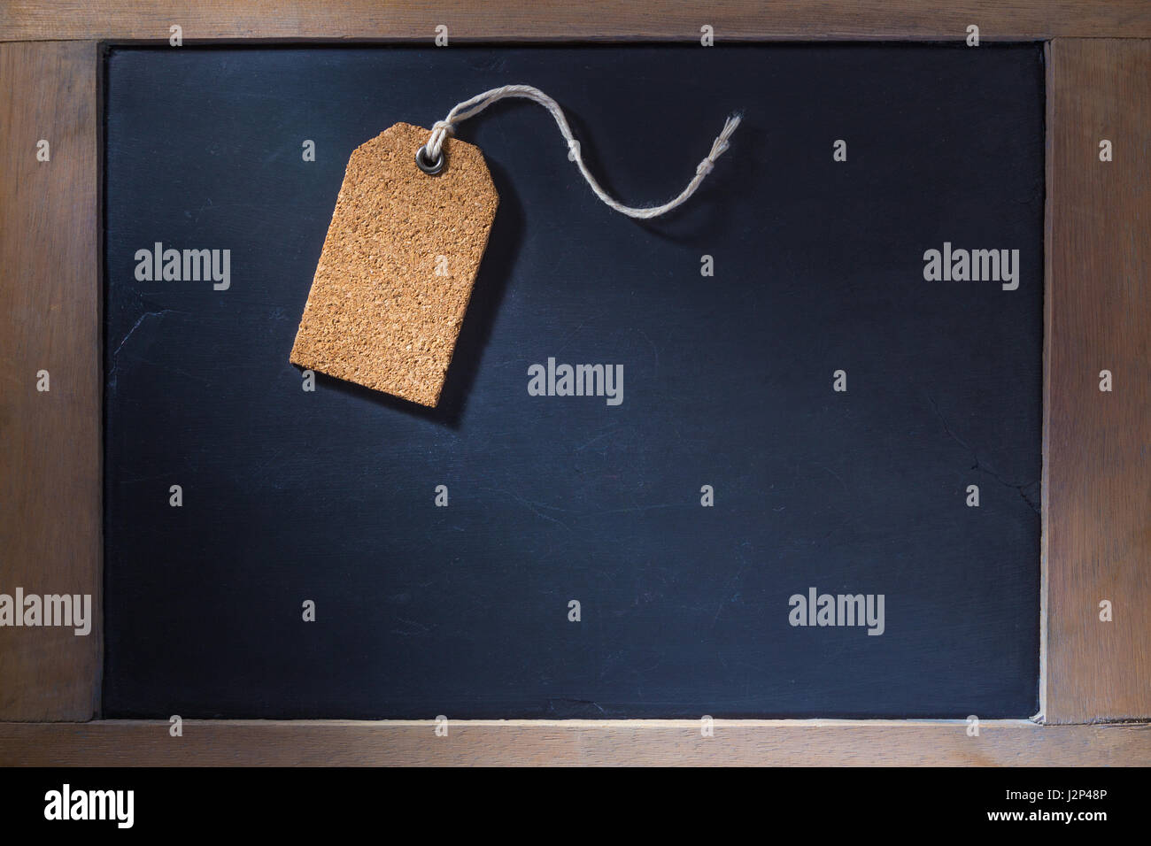 Empty cork tag su piccola lavagna con cornice in legno duro, illuminazione con ombre dure Foto Stock