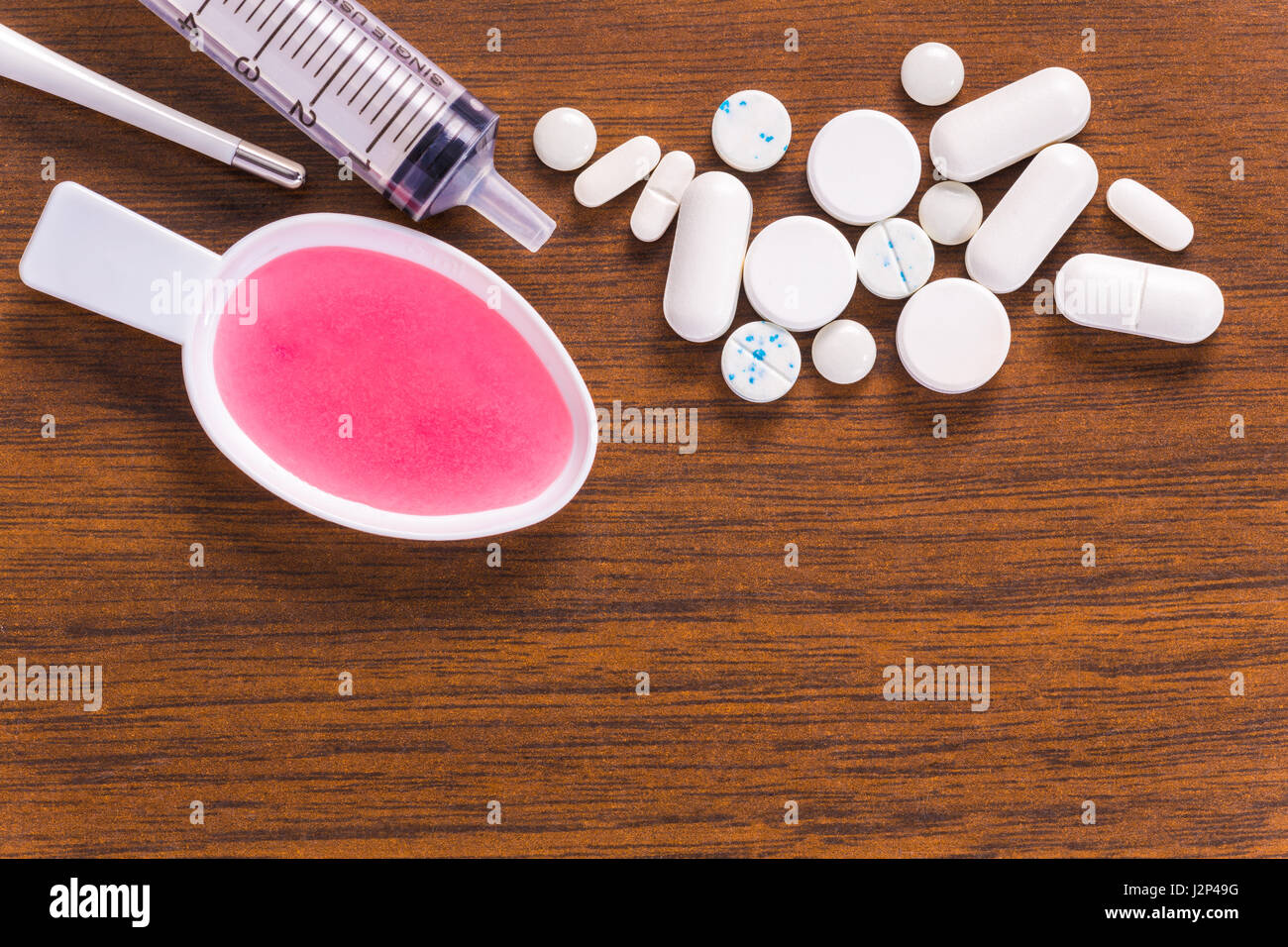 Pila di pillole di bianco, il termometro digitale, la siringa e la medicina liquida in plastica cucchiaio, tutti sulla tavola di legno Foto Stock