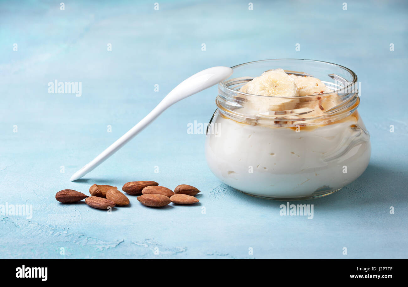 Yogurt di mandorla con banana, miele in un vasetto di vetro su uno sfondo blu Foto Stock