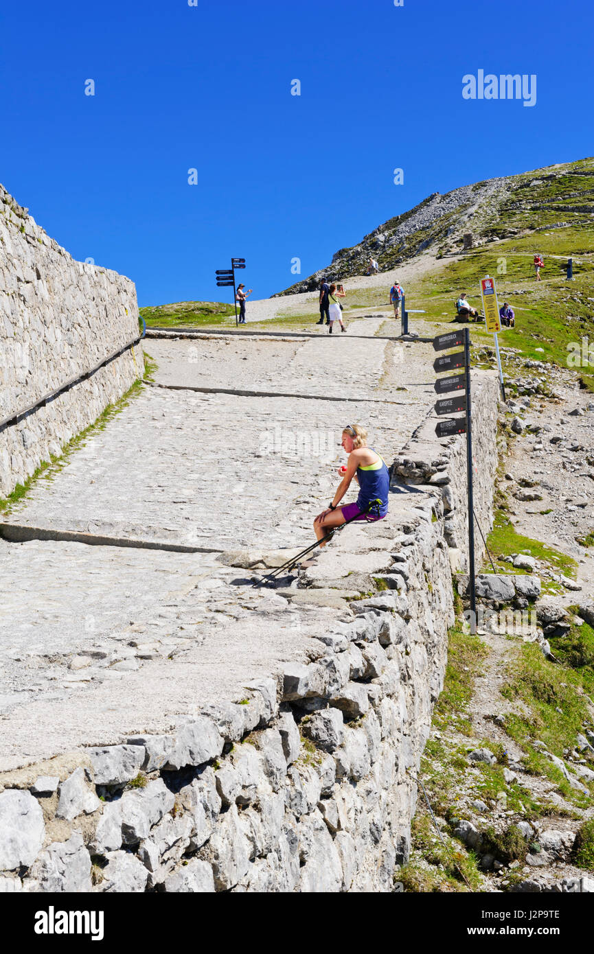 Un escursionista prendendo una pausa seduta una piccola parete rocciosa sulla cima della montagna Hefelekar, Tirolo, Austria Foto Stock