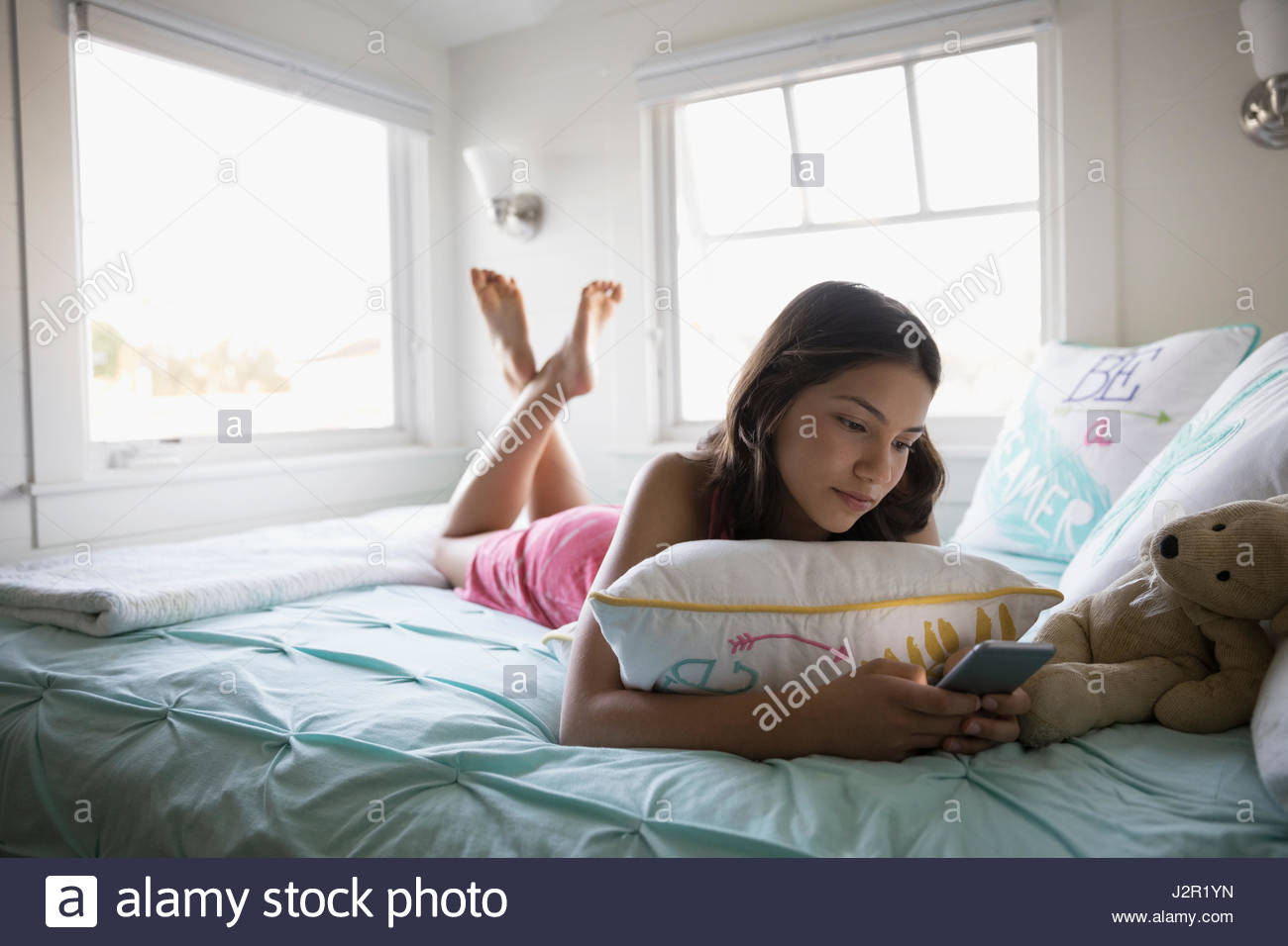 Ragazza adolescente con bretelle texting con smart phone sul letto Foto Stock