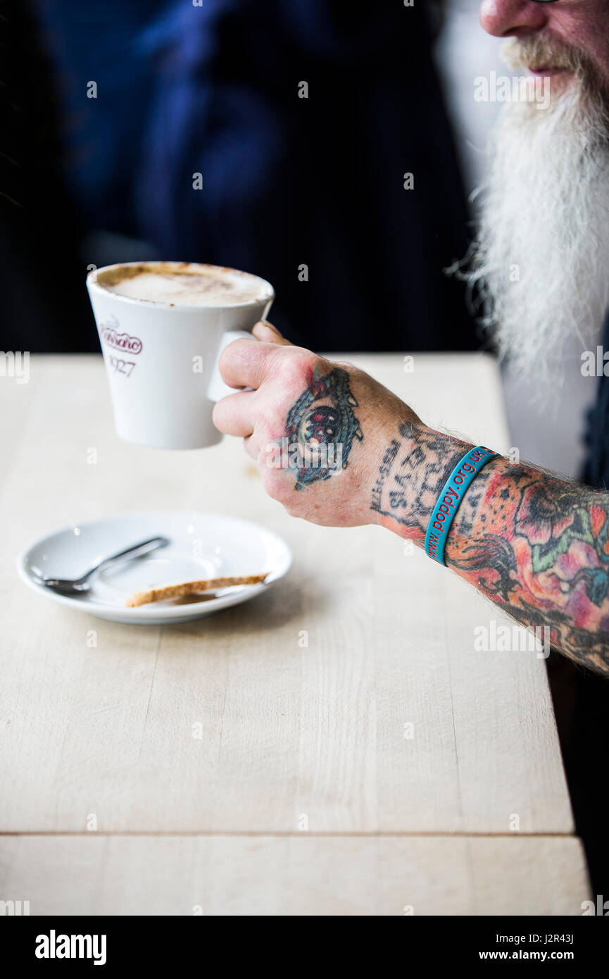 Una tazza di caffè tenuto in una mano tatuati tatuaggi disegni pausa caffè ristoro bevanda di caffè Foto Stock