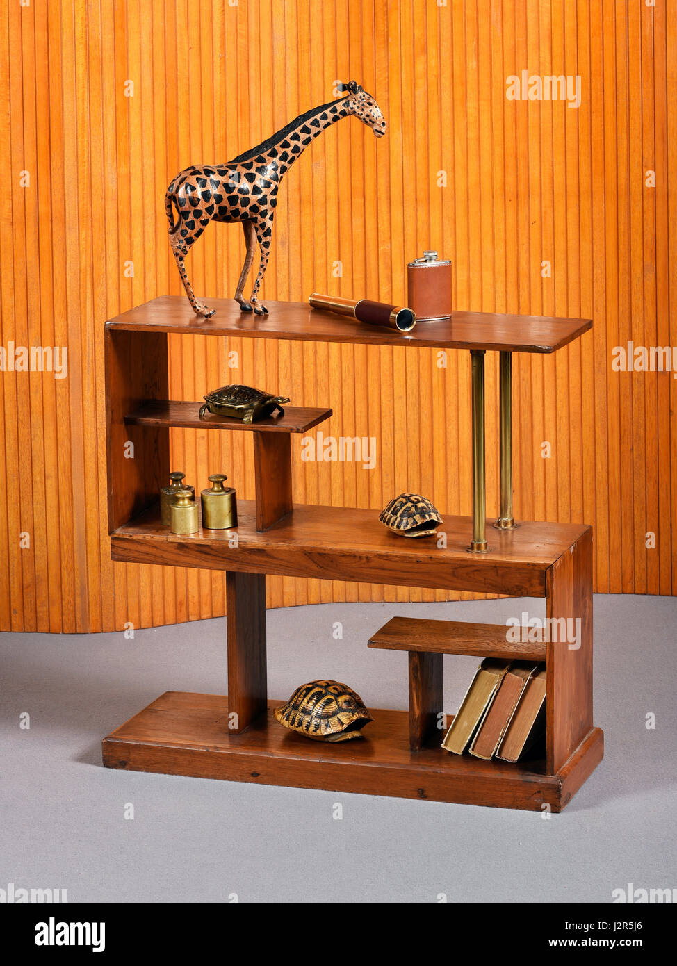 Piccola unità indipendente di legno rettangolare o libreria etagere con un souvenir in legno, giraffe libri tortoiseshells e pesi in ottone Foto Stock