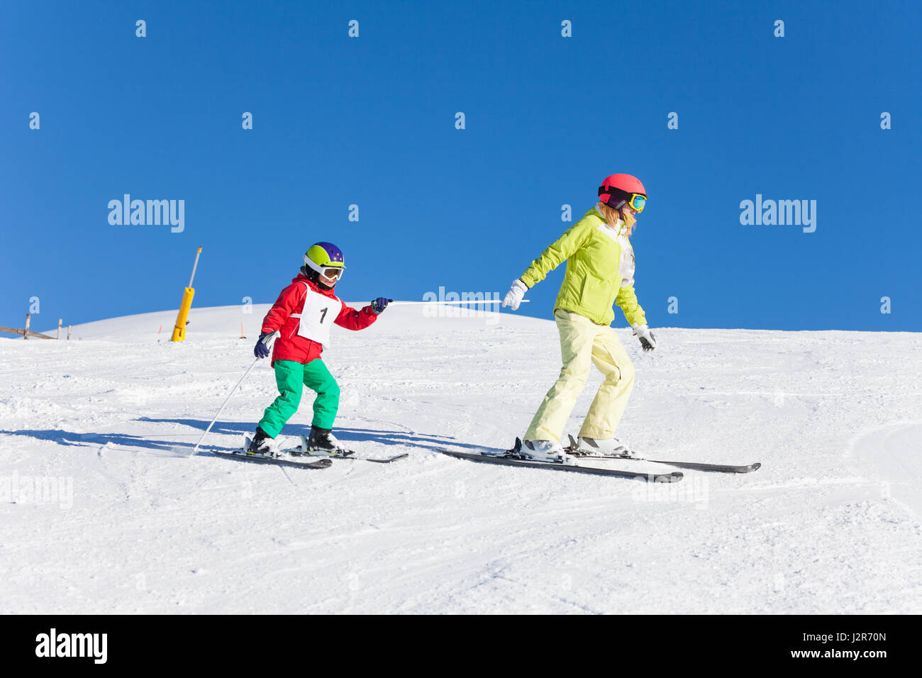 Sporty madre tirando il suo figlio di capretto su sci da un palo nella soleggiata giornata invernale Foto Stock