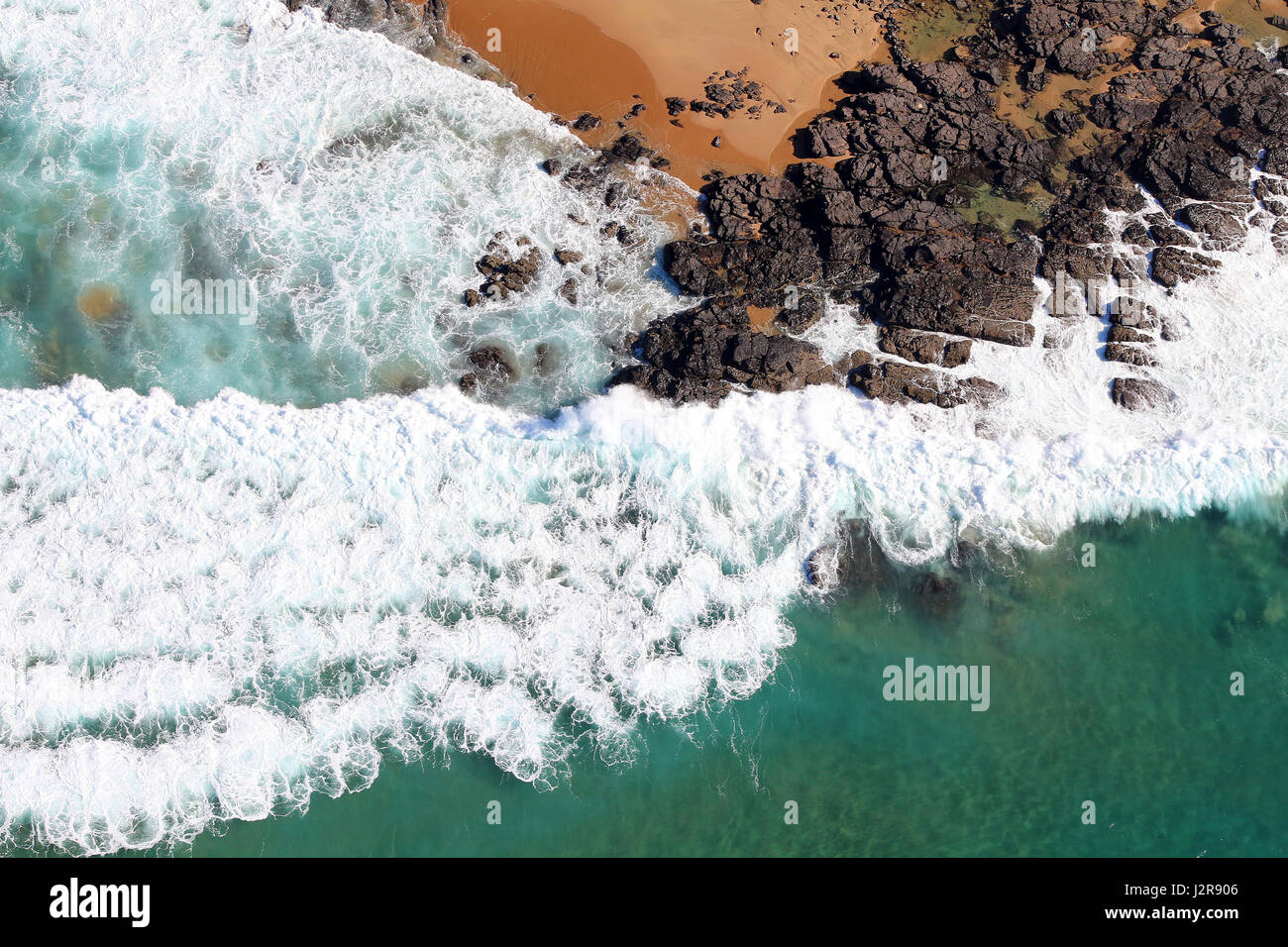 Una prospettiva aerea delle onde che si infrangono lungo una costa rocciosa. Foto Stock