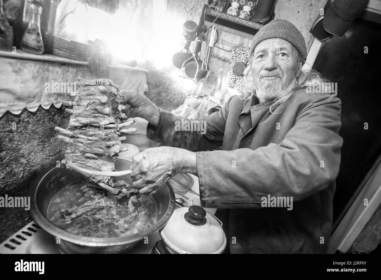 Un uomo vecchio punto di ebollizione a base di carne di maiale sulla stufa e tenendo in mano un pezzo di nervature. Foto Stock