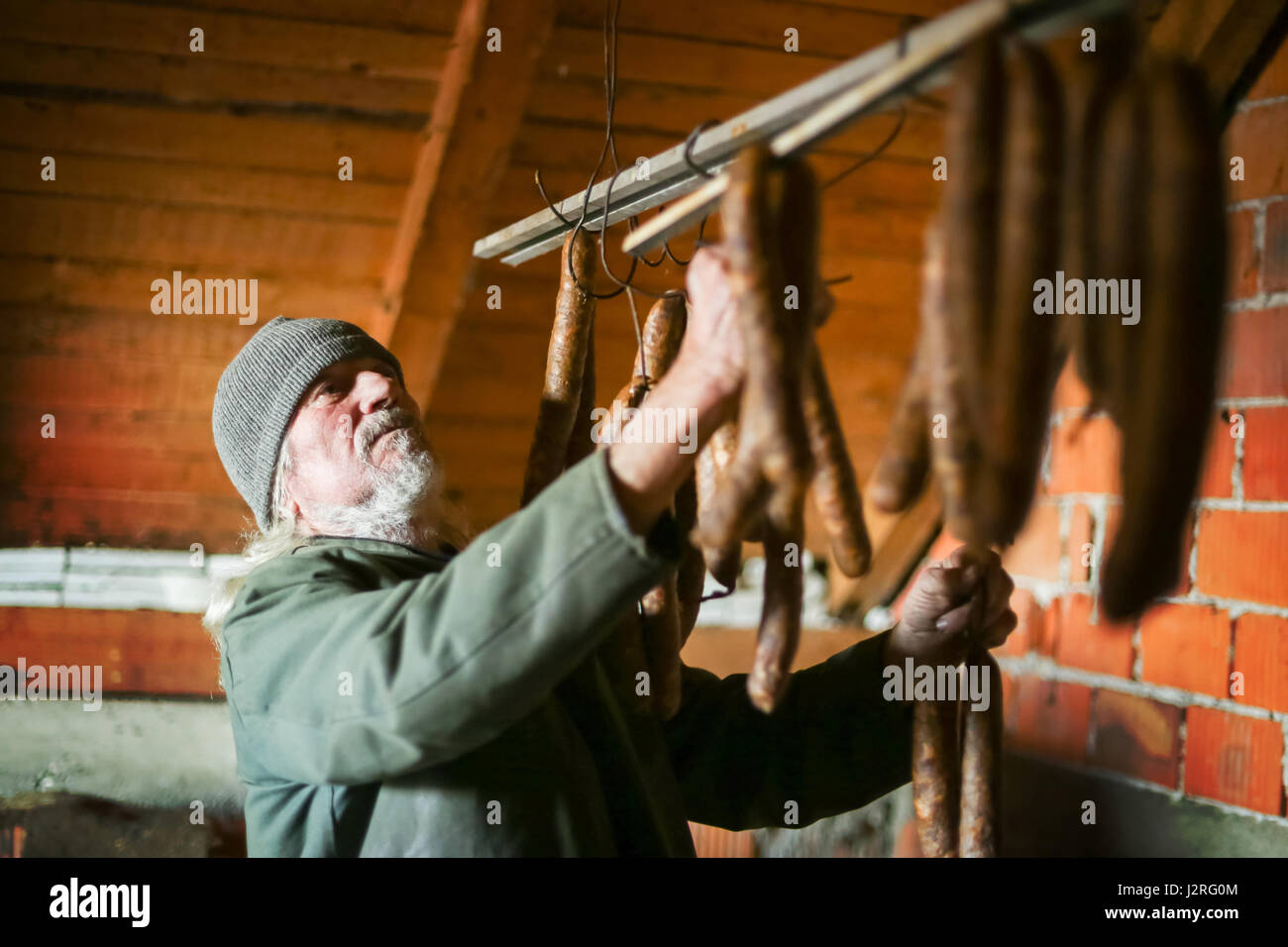 Un vecchio uomo controllo su asciutto salsicce appeso in attick. Foto Stock