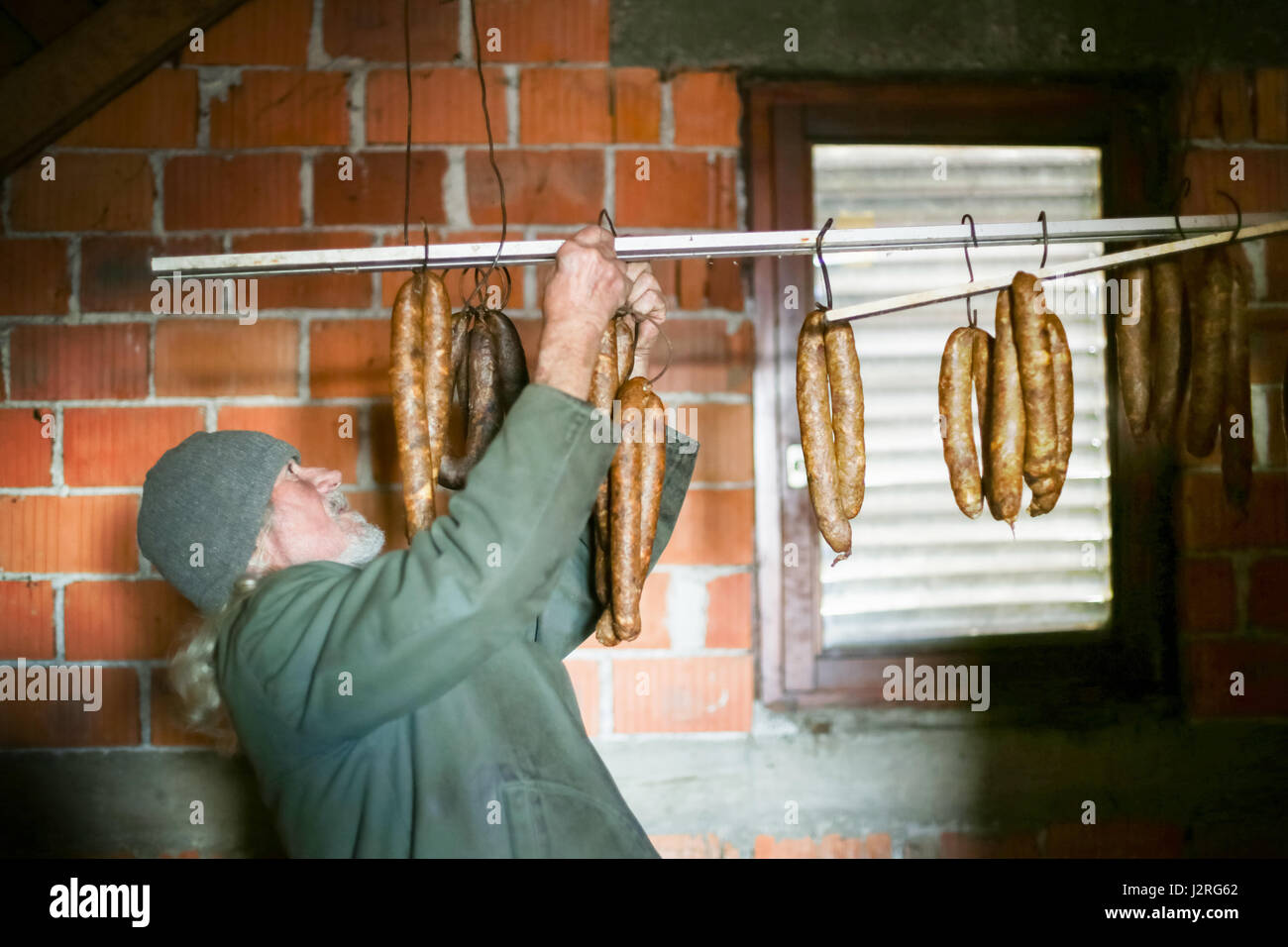 Un vecchio uomo controllo su asciutto salsicce appeso in attick. Foto Stock