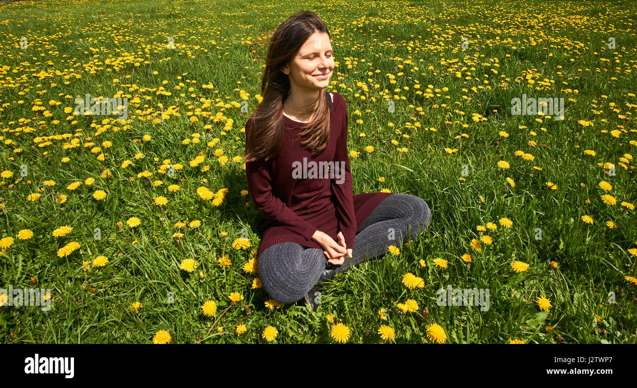 Bella giovane donna relax su un prato con molti denti di leoni sotto il sole di primavera. Sorridente con copyspace. Foto Stock