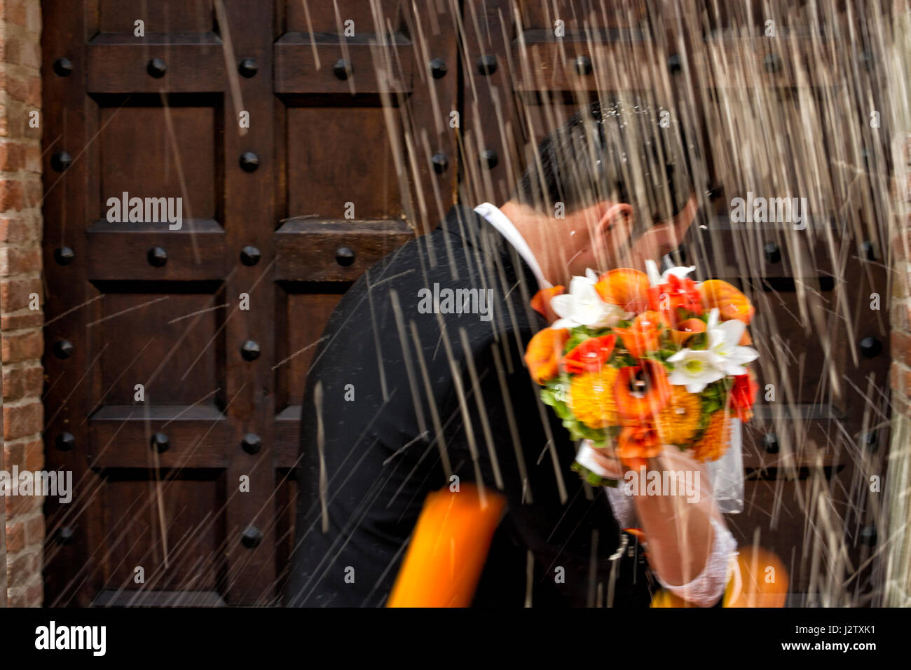 Sposa e lo sposo kiss con bouquet di fiori sotto la caduta di riso Foto Stock