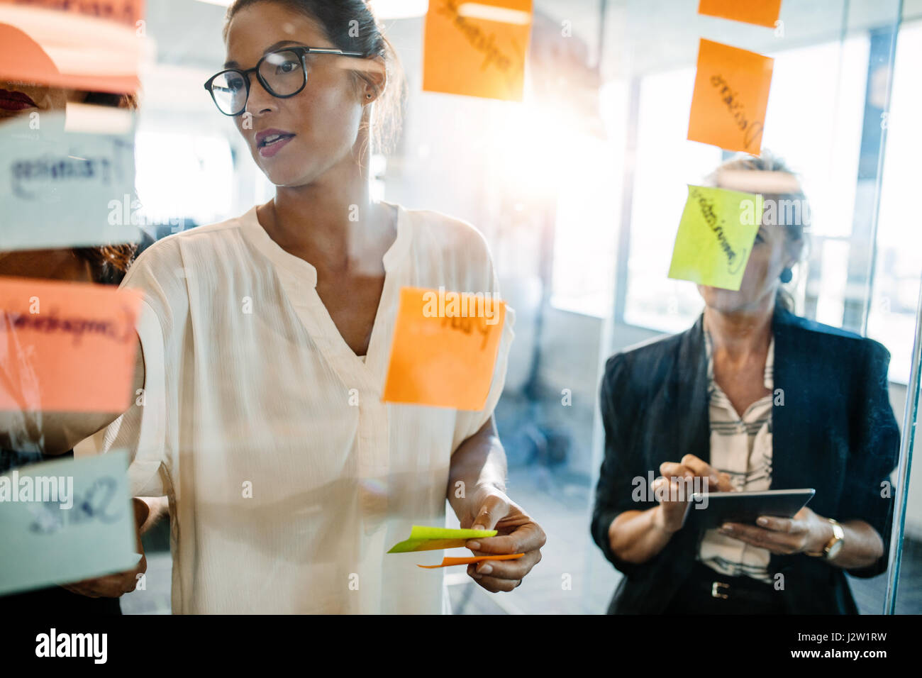 Ritratto di professionisti creativi cercando su un post-it parete e discutere. I dirigenti di sesso femminile in piedi presso l'ufficio dietro la parete in vetro con st Foto Stock