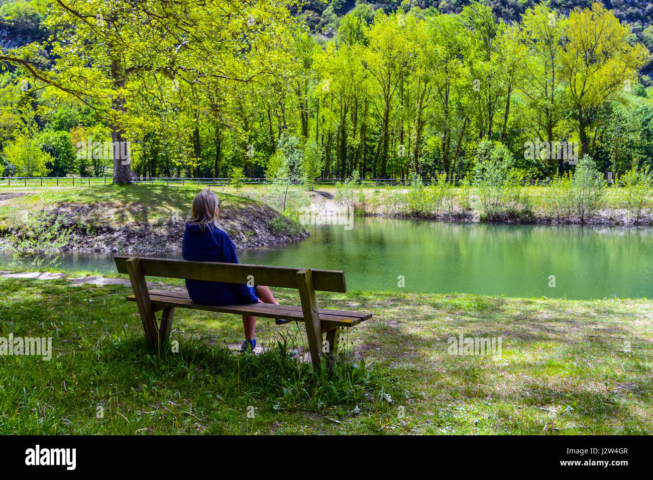 Vista posteriore della figura femminile sat su banco guardando il lago fiume Foto Stock