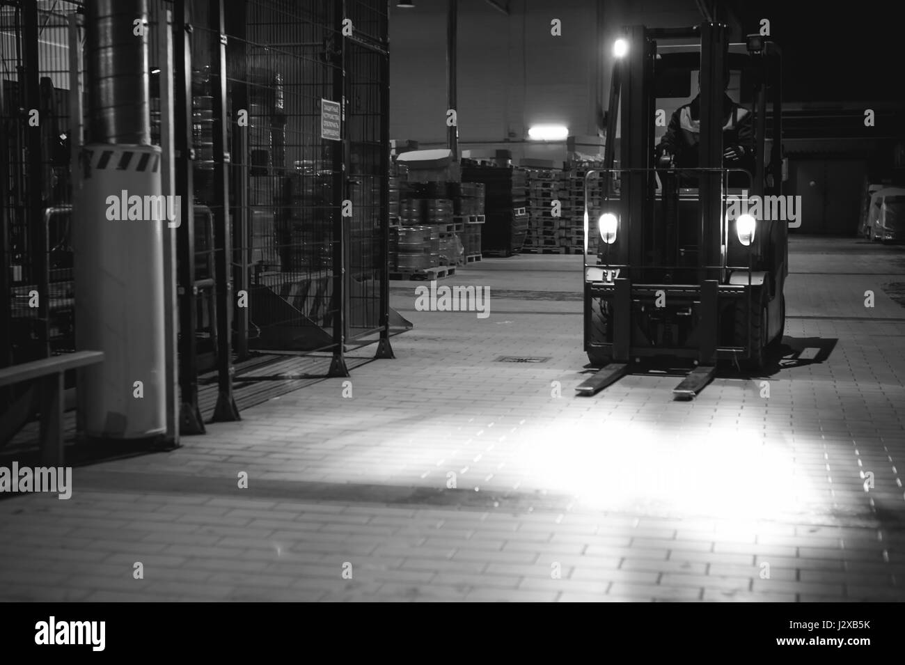 Dipendente del magazzino in tute vestiti, driver Reachtruck occupato a lavorare sulla logistica spostando sul caricatore su pallet con barili di birra sulla linea di fabbrica per pro Foto Stock