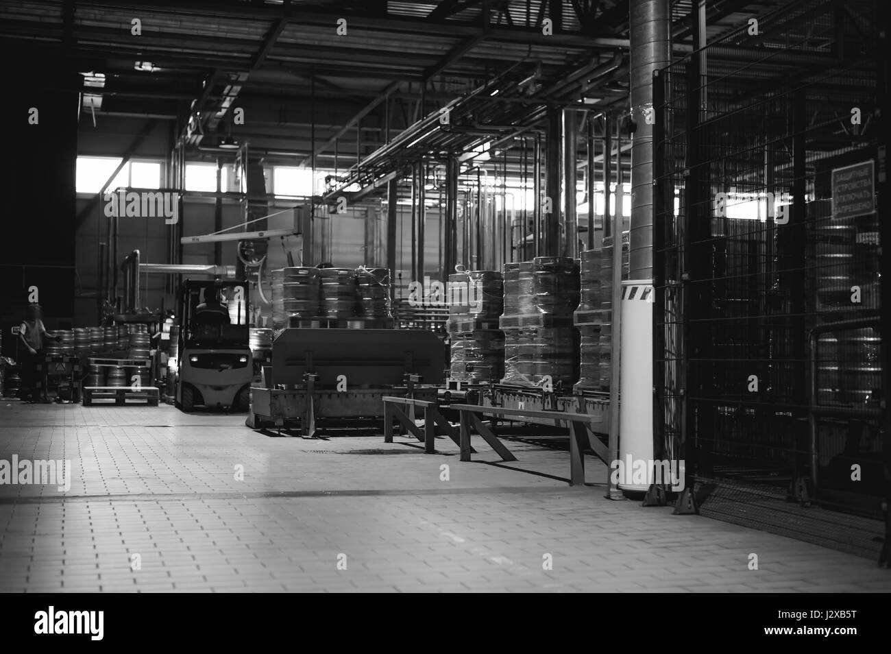 Dipendente del magazzino in tute vestiti, driver Reachtruck occupato a lavorare sulla logistica spostando sul caricatore su pallet con barili di birra sulla linea di fabbrica per pro Foto Stock