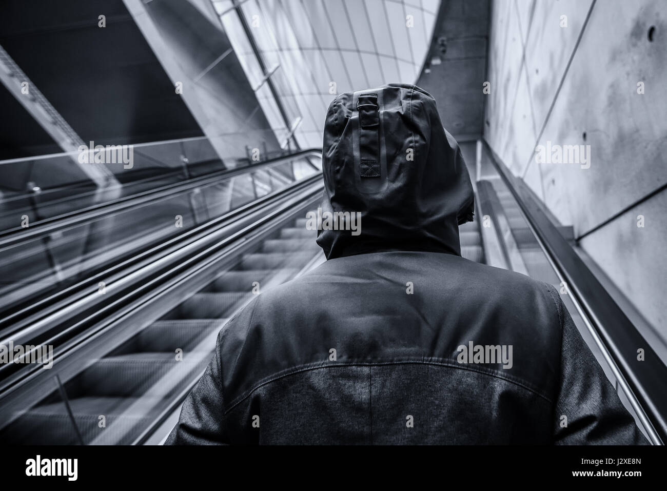 Irriconoscibile incappucciati persona sullo spostamento di escalator in moderno urbano circostante interno,immagine monocromatica con il fuoco selettivo Foto Stock