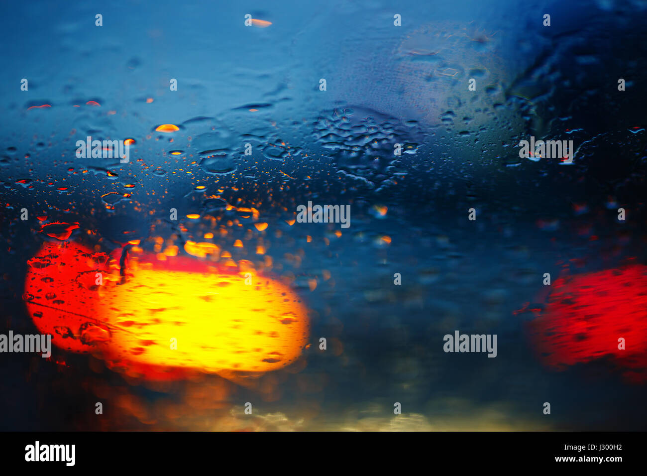 Gocce di pioggia sul vetro per auto con semaforo , concentrarsi sulle gocce di pioggia Foto Stock