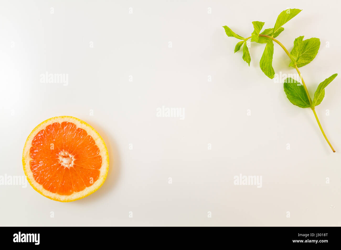 Vista superiore della singola fetta di pompelmo e foglie di menta su sfondo bianco. Immagine minimalista di stile con copia spazio per il testo Foto Stock