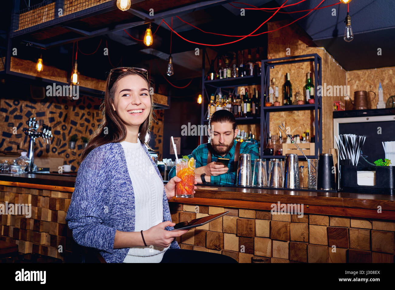 Una ragazza con cocktail di sorrisi con la compressa dietro il contatore al b Foto Stock