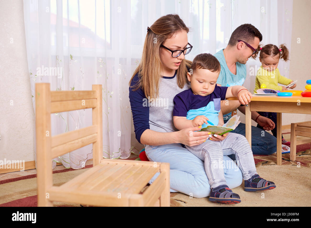 La mamma e il padre di leggere un libro con i bambini in camera Foto Stock