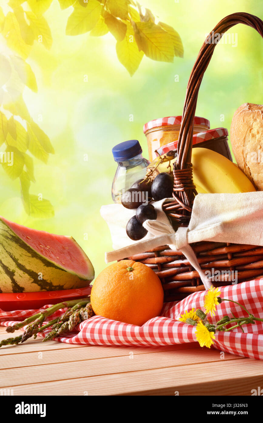 Picnic a cesto in vimini con il cibo sulla tavola nel campo con il verde della natura dello sfondo. Il concetto di picnic vicino. Vista frontale. Composizione verticale. Foto Stock