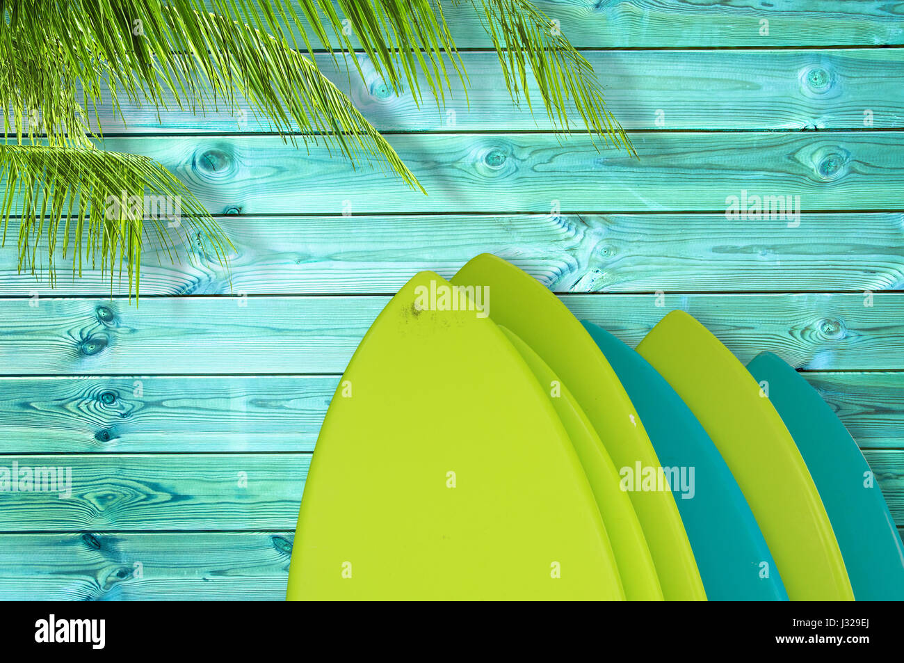 Pila di colorate tavole da surf su un blu tropicali doghe in legno sfondo con Palm tree Foto Stock