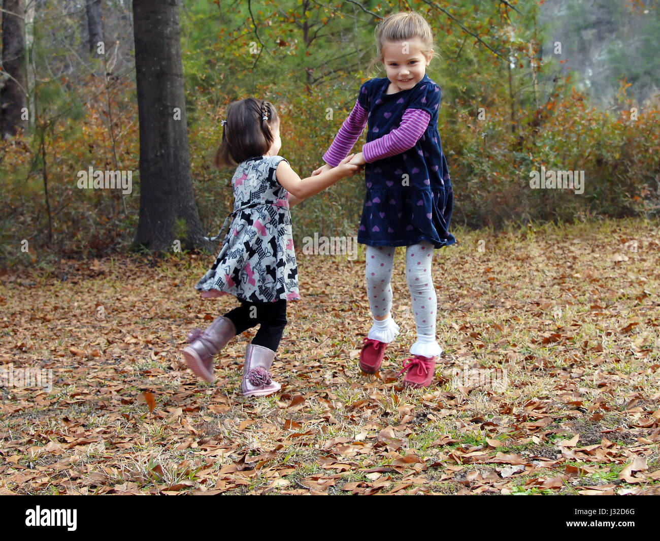 Due bambine tenere mani e swing in cerchi. Stanno giocando i giochi all'aperto nella caduta foglie. Foto Stock