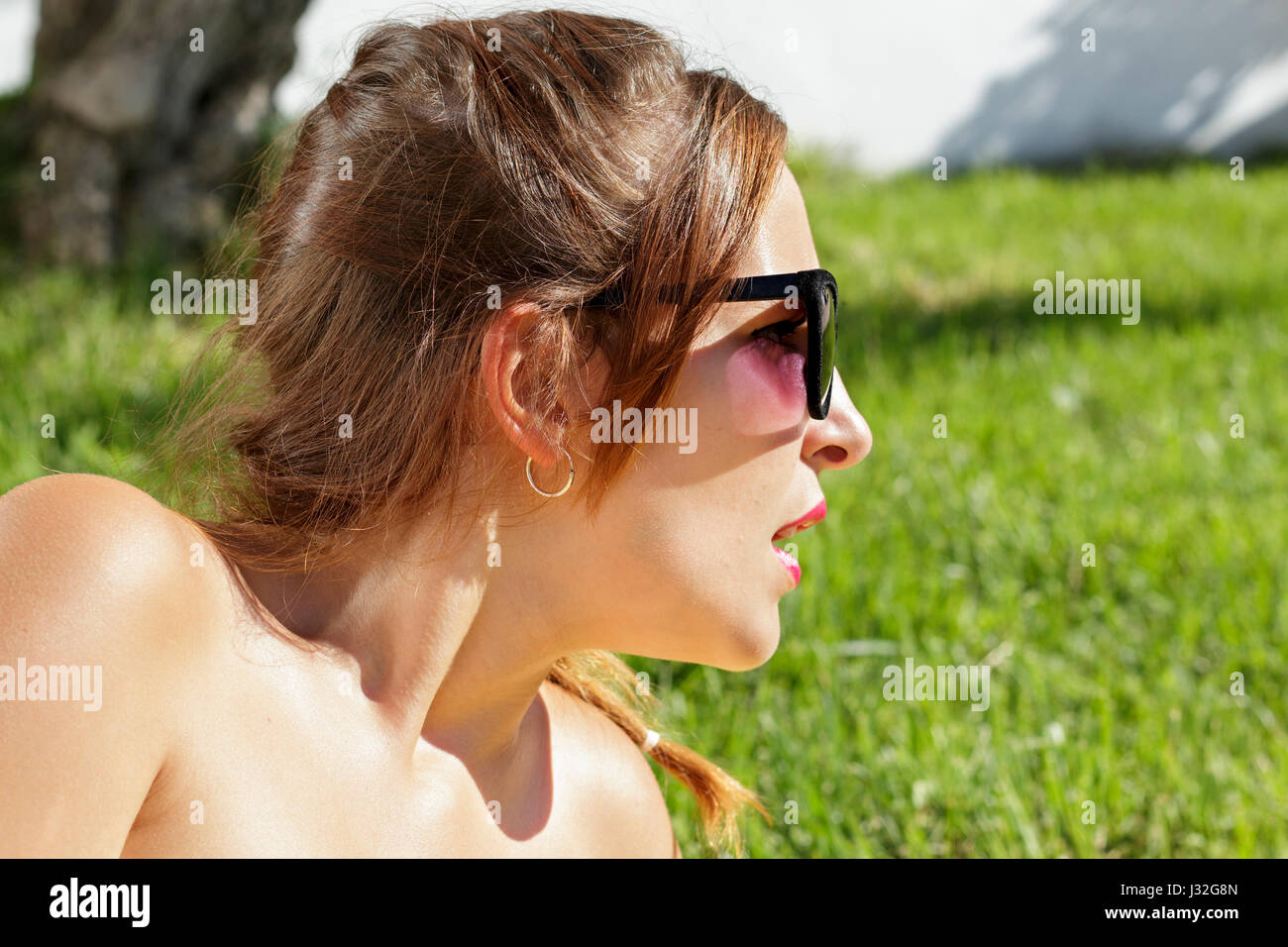 Giovane donna con occhiali da sole che giace sull'erba sembra sorpreso a destra Foto Stock