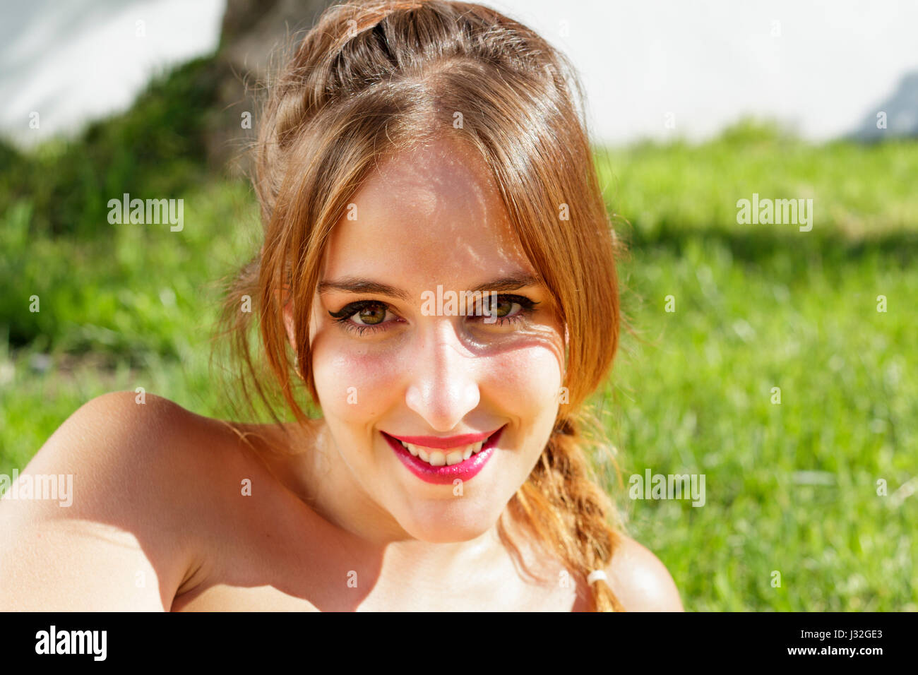 Bella donna con gli occhi verdi sorride alla fotocamera mentre è sdraiato sull'erba Foto Stock