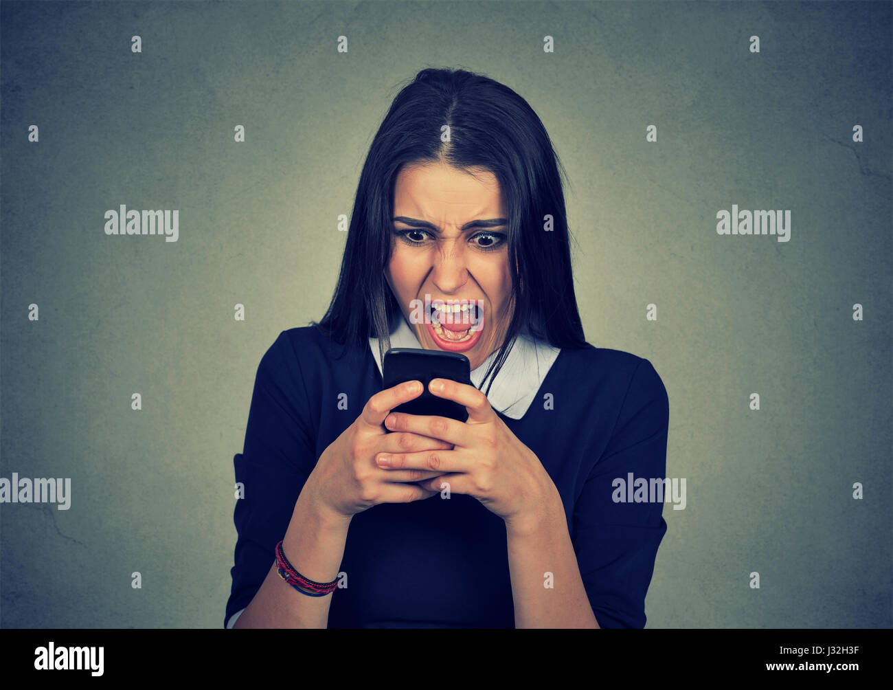 Ritratto arrabbiato giovane donna urlando sul telefono cellulare isolato su sfondo grigio. Le emozioni negative sentimenti faccia atteggiamento di espressione Foto Stock
