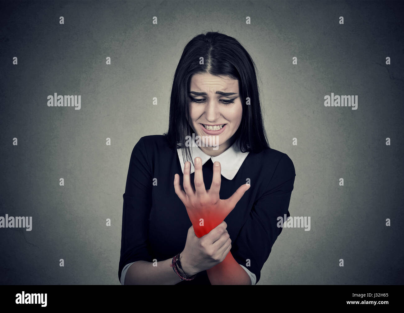 Giovane donna mentre tiene il suo polso doloroso colorati in rosso isolato sul muro grigio Sfondo. Lo stiramento dolore Foto Stock