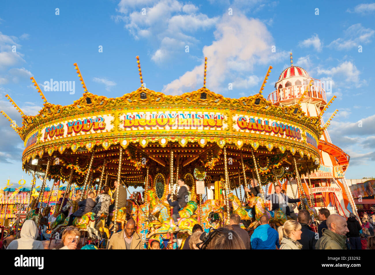 Una folla di persone intorno a un tradizionale fairground ride. A Merry Go Round in serata sole alla fiera d'oca, Nottingham, Inghilterra, Regno Unito Foto Stock