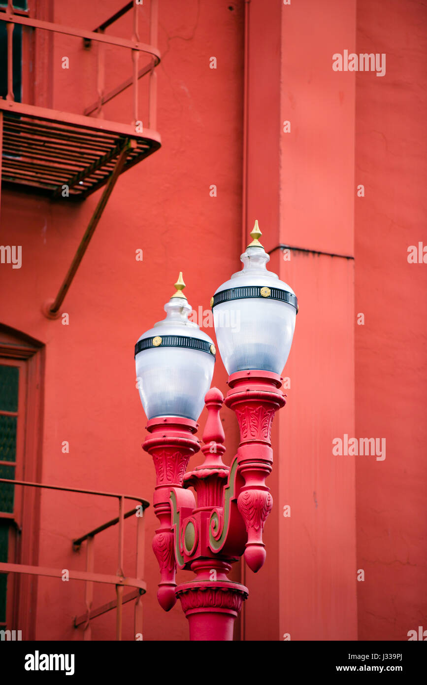 Classico ed elegante lampione rosso con due traslucido satinato vaso scanalato con bordo in metallo sullo sfondo parete rossa di un alto edificio con balconi. Foto Stock