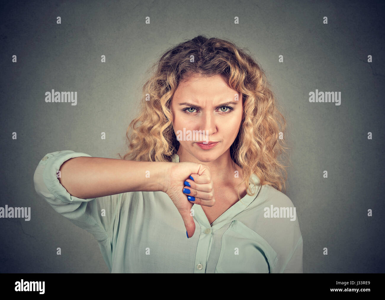 Donna che il pollice verso il basso gesto guardando con espressione negativa e riprovazione isolato su sfondo grigio Foto Stock