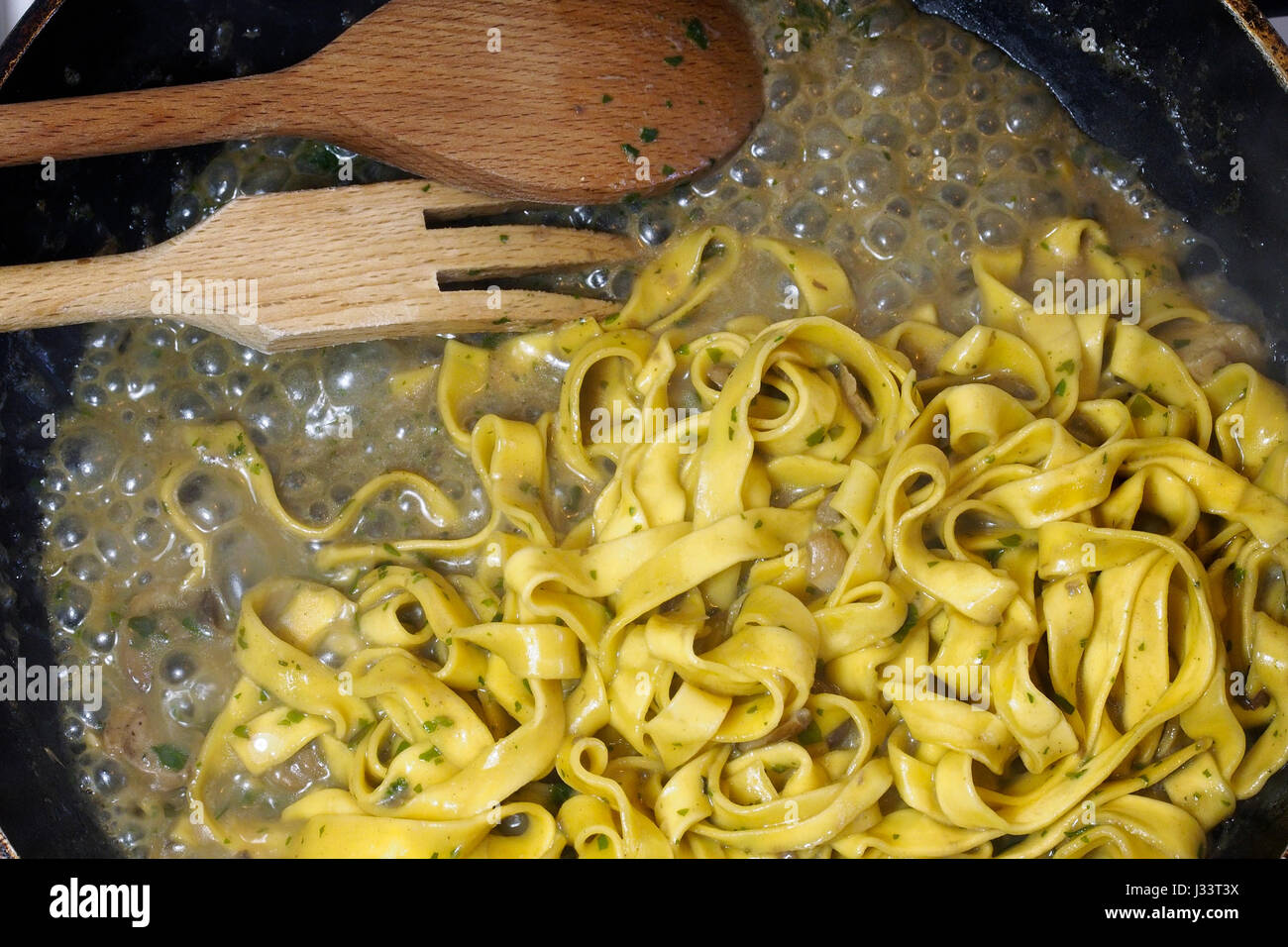 Tagliatelle di cottura, la pasta italiana, con funghi. Cucina in legno utensili utilizzati. Foto Stock
