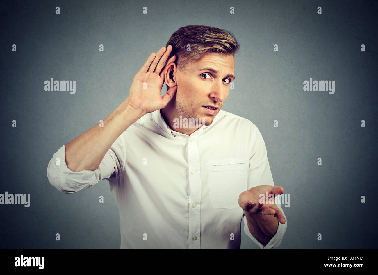 Infelice di udito collocando man mano sull'orecchio chiedere a qualcuno di parlare o ascoltare le cattive notizie, isolata su uno sfondo grigio. Emozione negativa fac Foto Stock