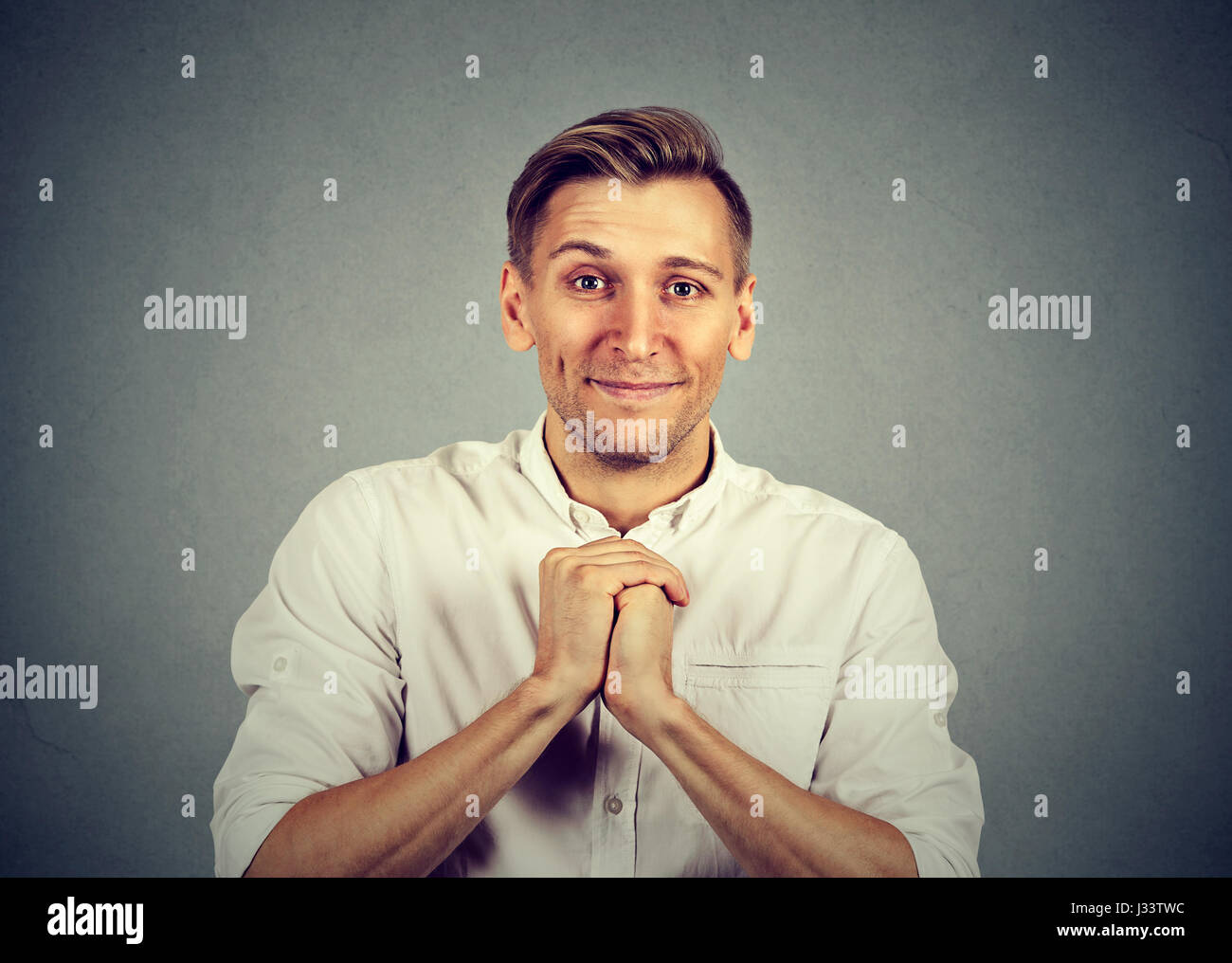 Tipo giovane uomo che mostra mani giunte, piuttosto si prega di isolati su sfondo grigio. Emozioni umane espressione facciale sentimenti, il linguaggio del corpo Foto Stock