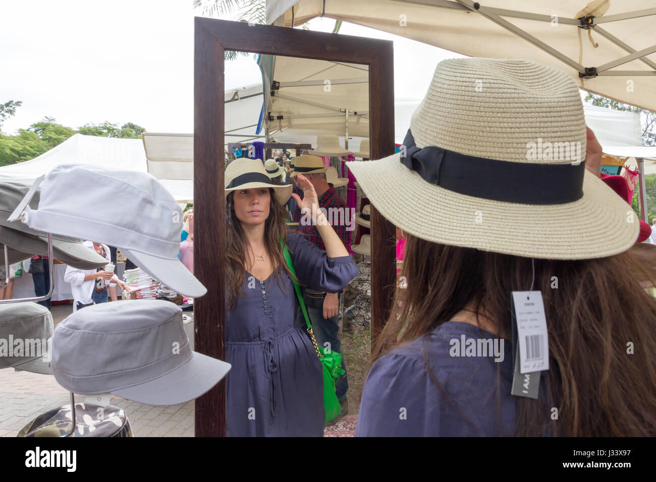 Giovane donna cercando su un cappello e guardando in uno specchio a mercati Eumundi, Queensland, Australia Foto Stock