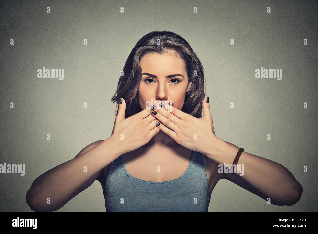 Closeup Ritratto di giovane donna la copertura con le mani la sua bocca isolato sul muro grigio sfondo Foto Stock