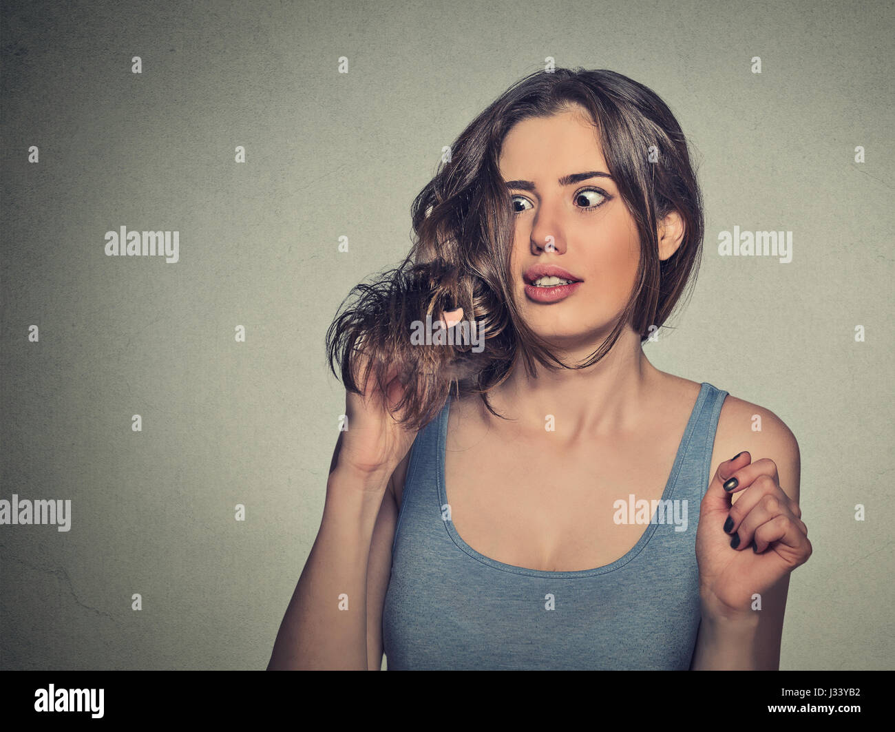 Closeup frustrato scioccato giovane donna infelice con il suo nuovo taglio di capelli, notato Finisce Spalato isolato su sfondo grigio. Volto umano espressione di emozione. B Foto Stock