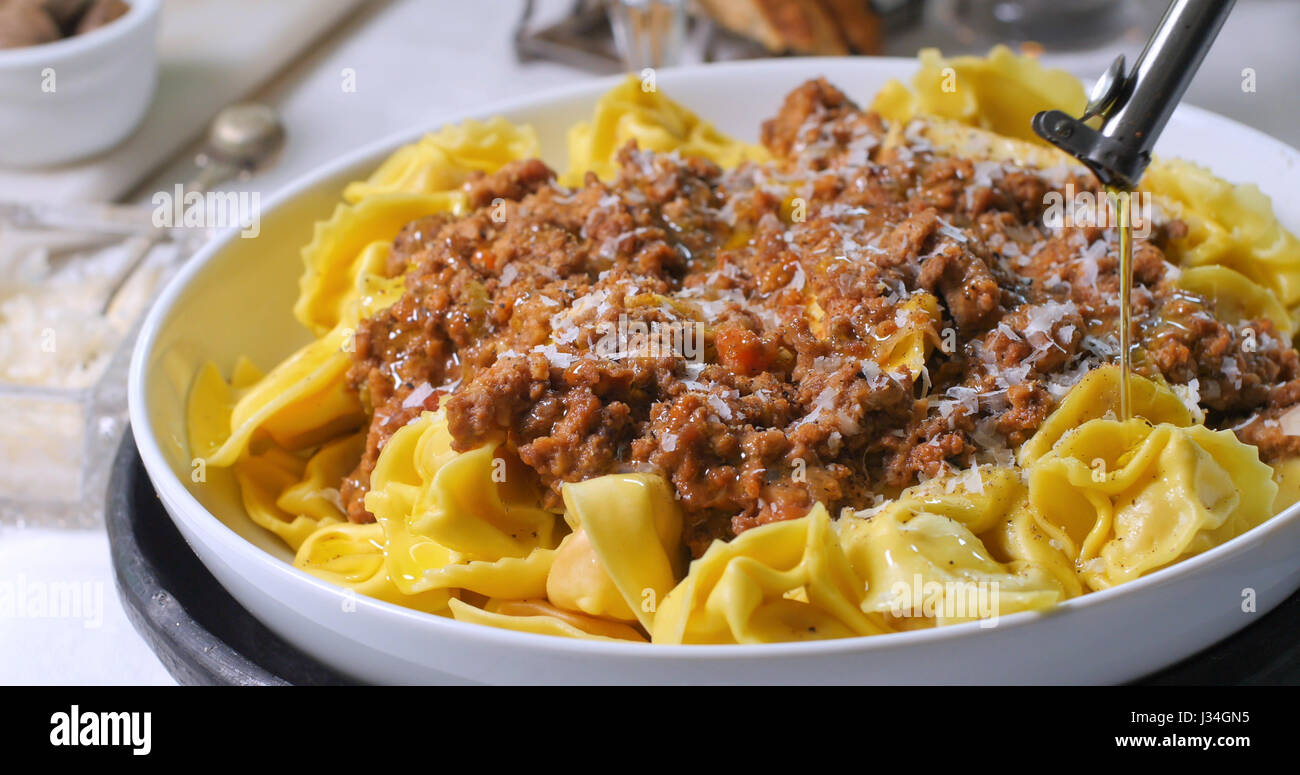 Versando l'olio d'oliva sulla deliziosa steamy tortellini in salsa bolognese Foto Stock